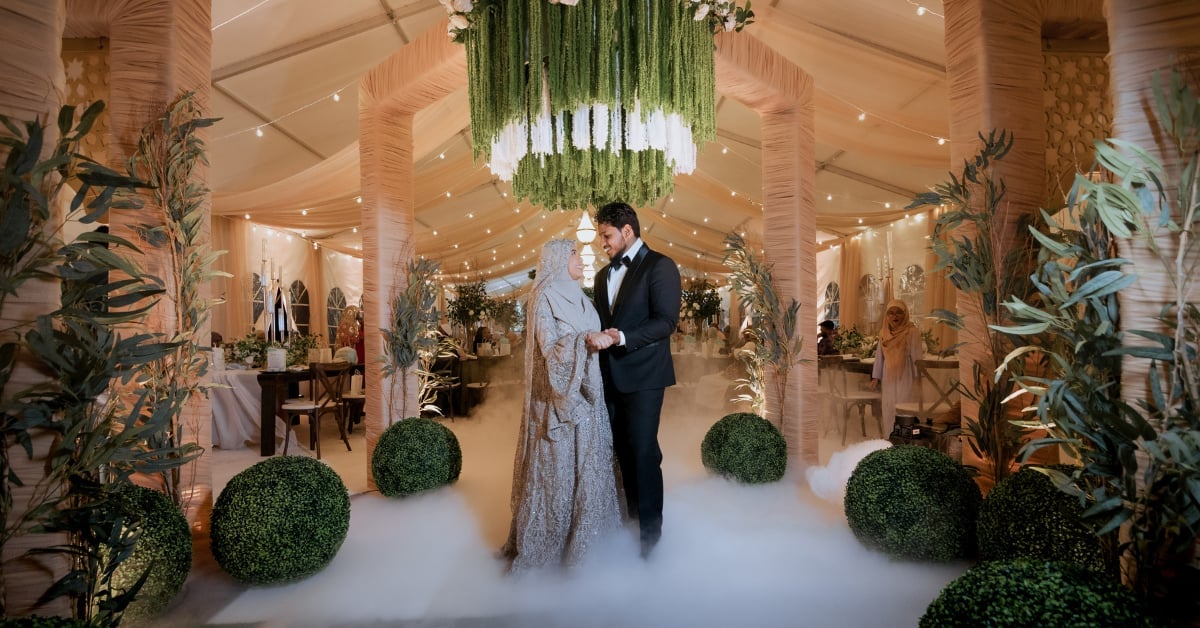 Elegant couple walking through a luxurious venue with hanging greenery, potted plants, and dramatic lighting