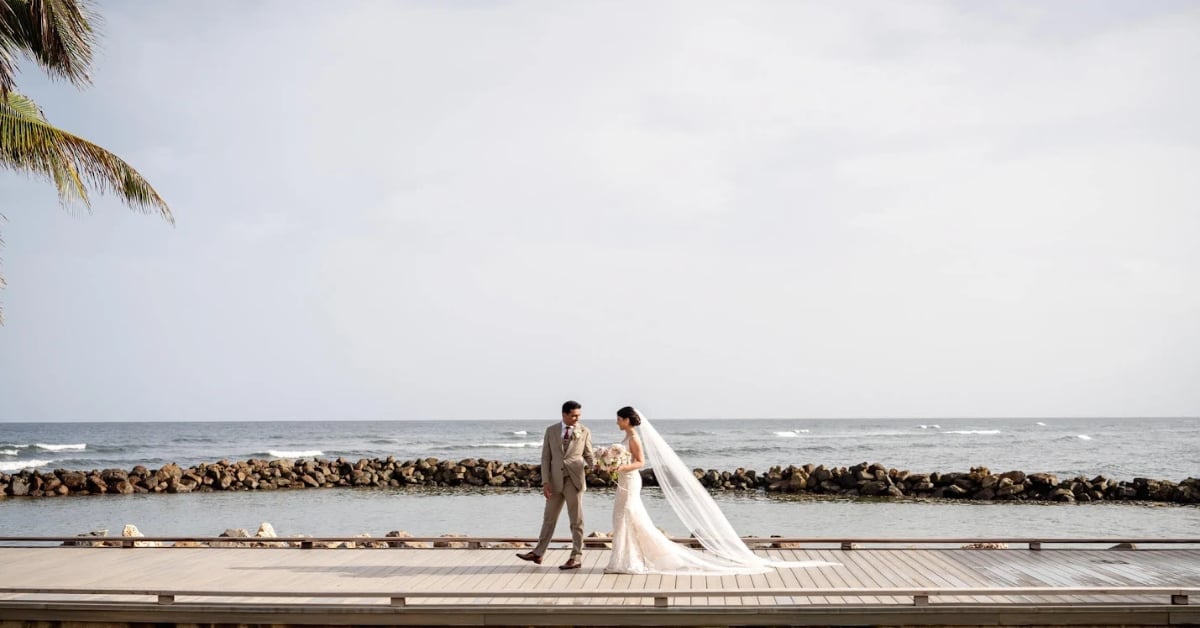 Bride and groom walking on wooden pier by ocean during wedding ceremony on overcast day