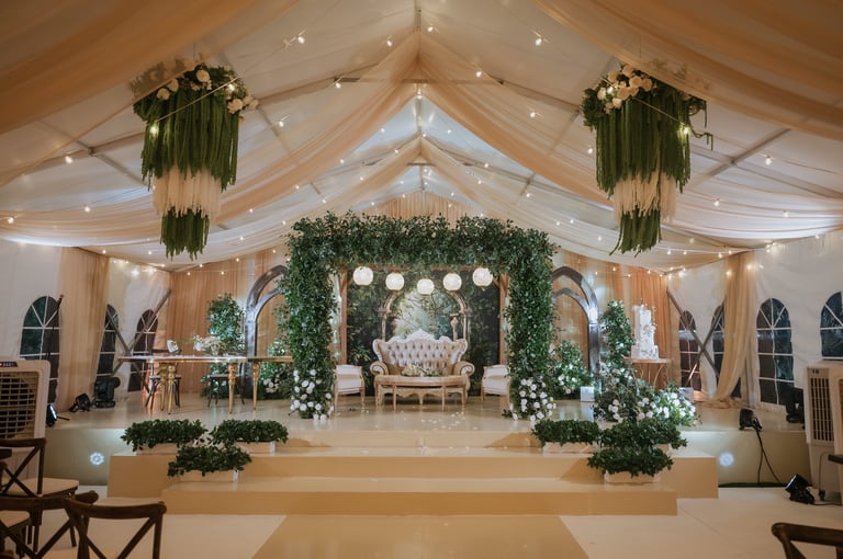 Elegant wedding reception tent with floral-draped ceiling installations, greenery columns, and ornate seating arrangement on stage