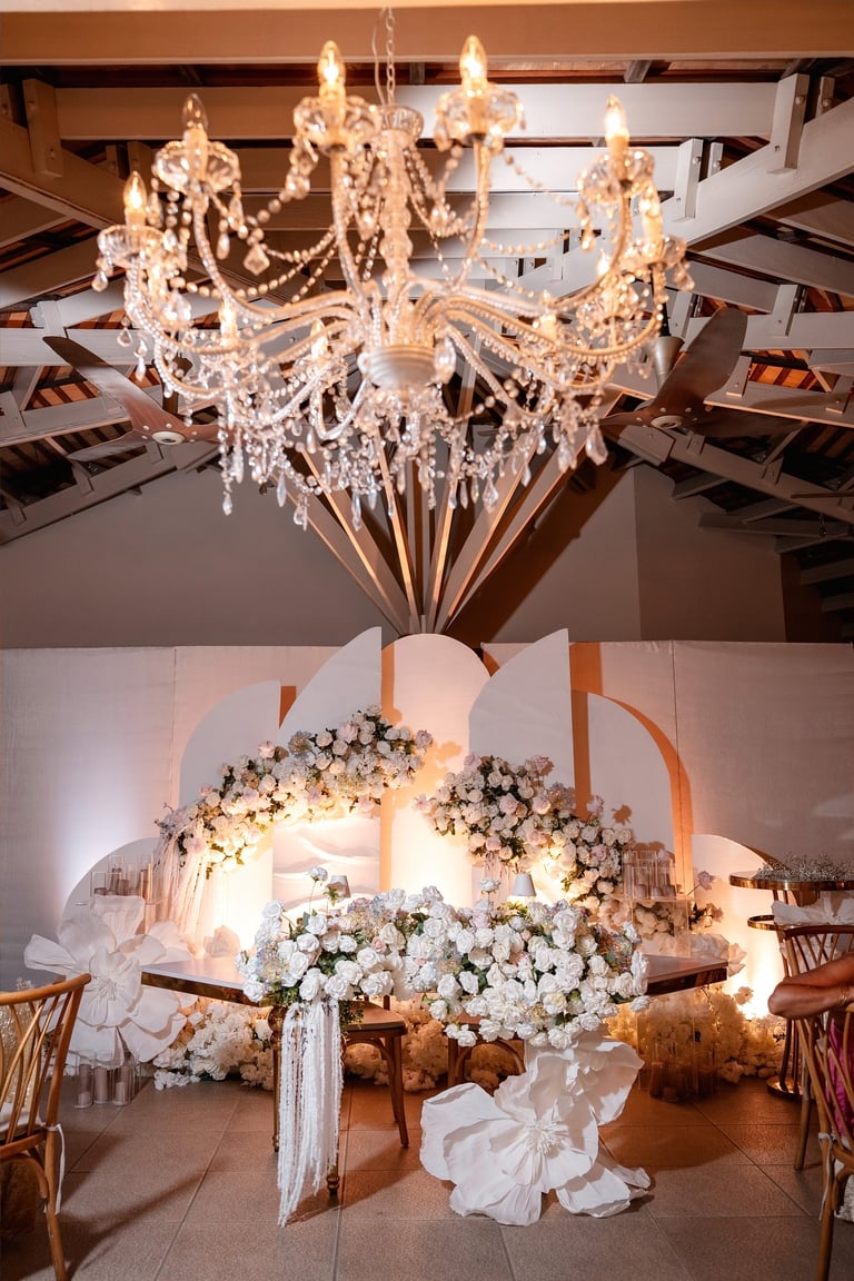 Crystal chandelier hanging above an ornate wedding altar decorated with white flowers and geometric arch structure