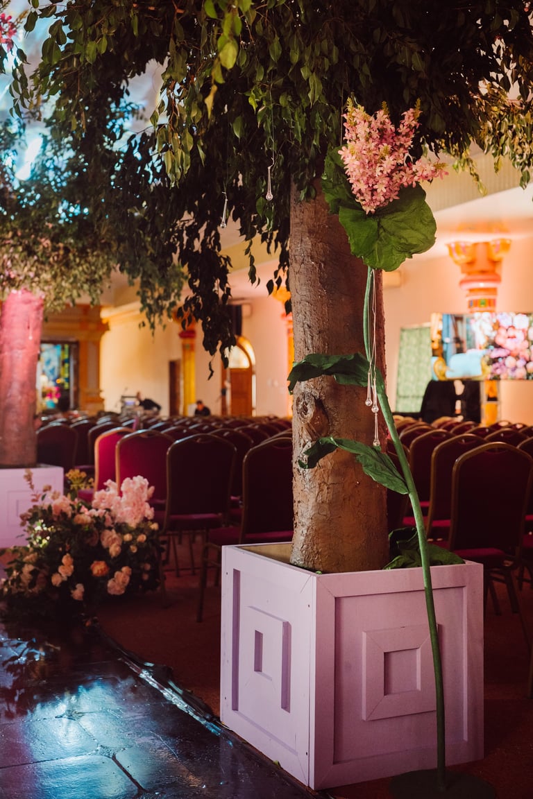 Tree with pink flowers in decorative planter inside colorful venue with burgundy seating and floral arrangements