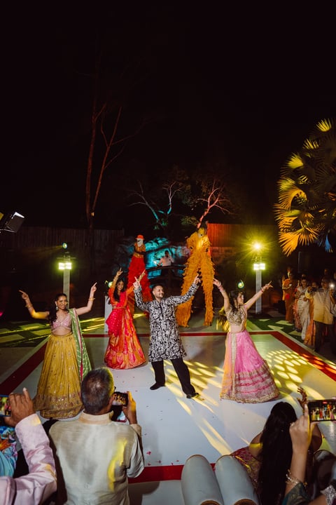Night celebration with people in traditional Indian attire dancing on lit stage surrounded by spectators and decorative lighting