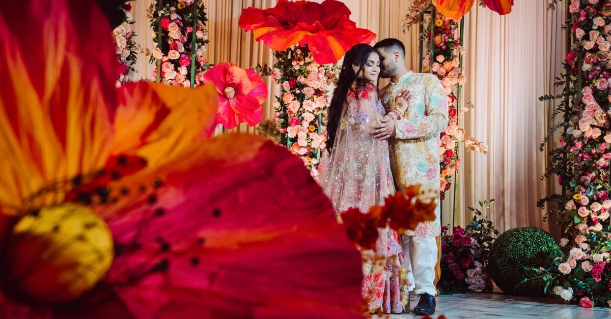 Couple embracing in ornate floral garden setting with vibrant red and pink flowers surrounding them