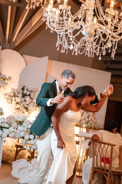 Couple dancing at elegant wedding reception with crystal chandeliers and white floral decorations